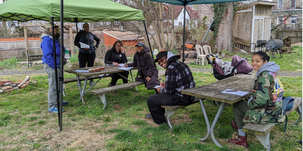 photo: warmly dressed small group at picnic tables under pop-up shelters