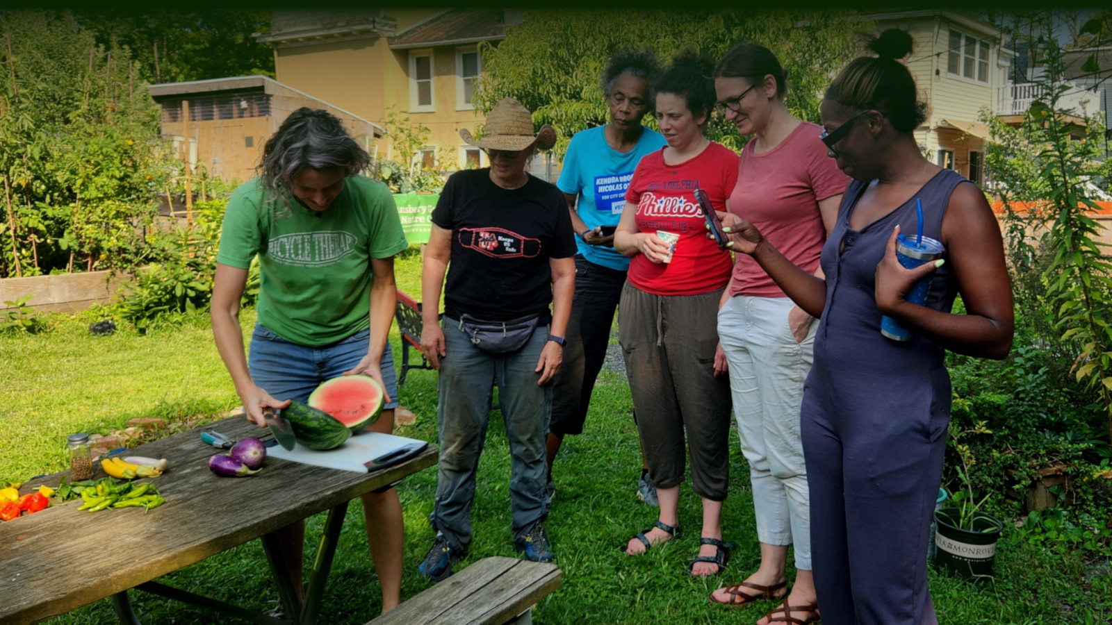 photo: people watching a woman cut a watermelon on a picnic table